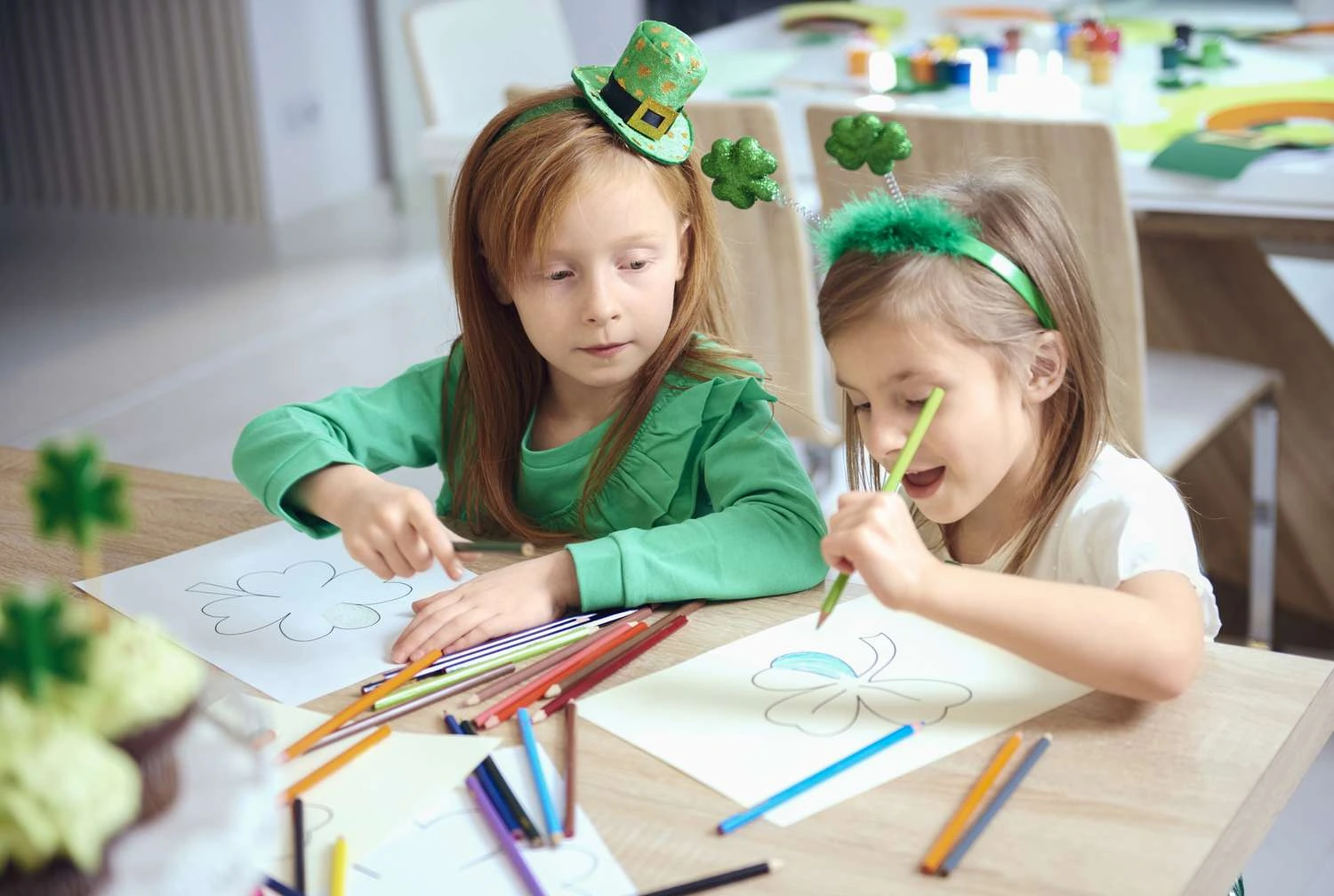 Two young girls in green outfits are focused on drawing on sheets of paper, showcasing their creativity and imagination.