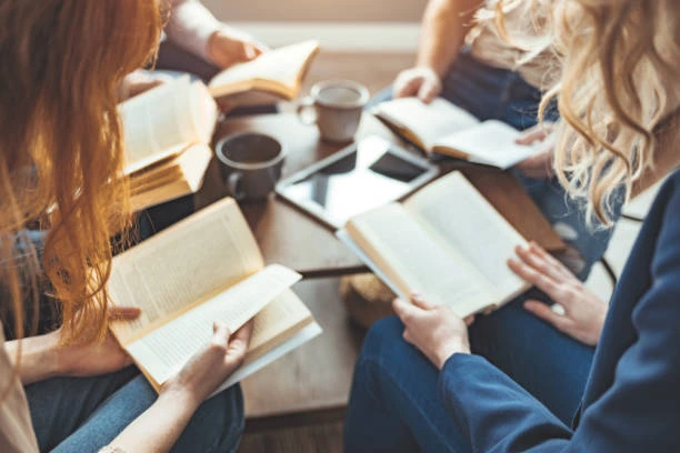 A diverse group of individuals engaged in discussion while seated around a table filled with books.