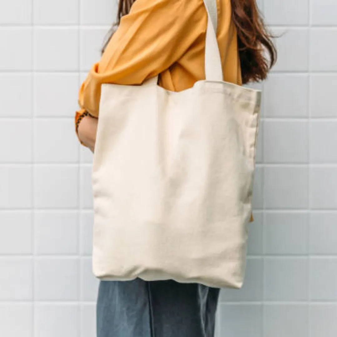 A woman in an orange shirt holds a tote bag over one shoulder.