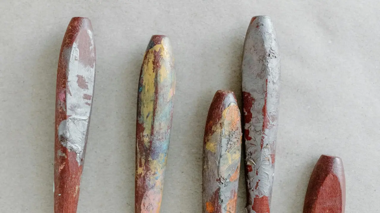 Five worn, colorful wooden sculpting tools, showing paint residue and varying textures, arranged on a light gray background.