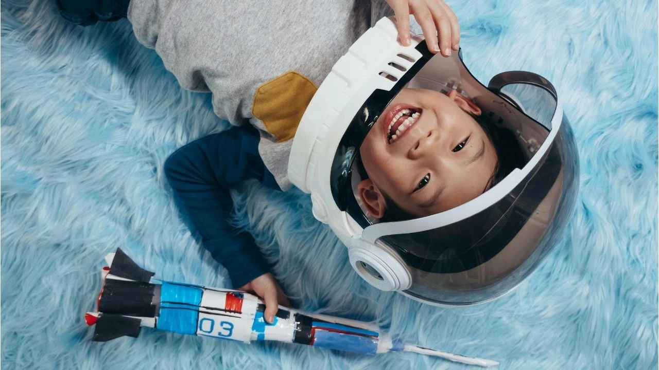 A young boy in a space helmet holds a toy rocket, embodying a playful astronaut ready for an imaginative adventure.