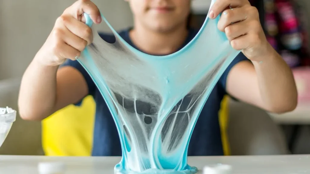 A young boy is mixing ingredients to create blue slime in a bowl, focused on his fun science project