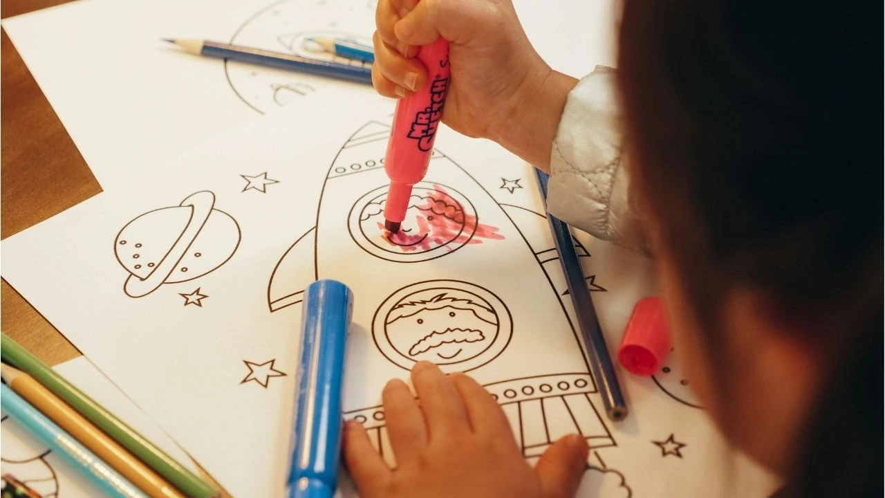 A child draws a colorful rocket on a piece of paper, showcasing creativity and imagination.