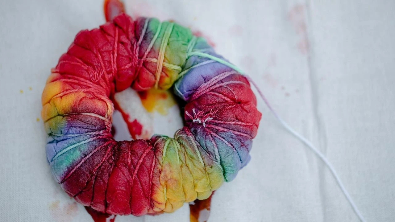 A piece of dyed fabric, rolled into a donut shape, with a string tied to it, resting on a white surface.