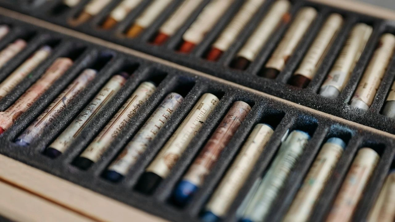A wooden case containing a variety of colored pastels arranged neatly inside.