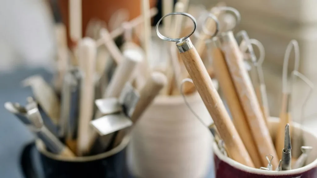 Close-up of various pottery tools with wooden handles in containers. The tools are in focus, creating a creative, artistic, and organized atmosphere.