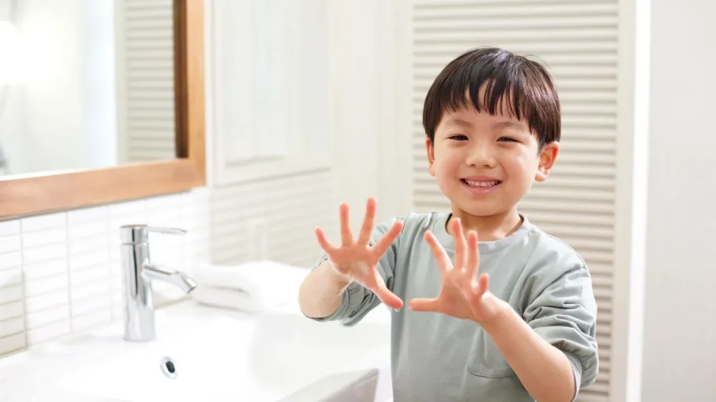 A little boy, standing in front of a sink and showing off his freshly washed hands.