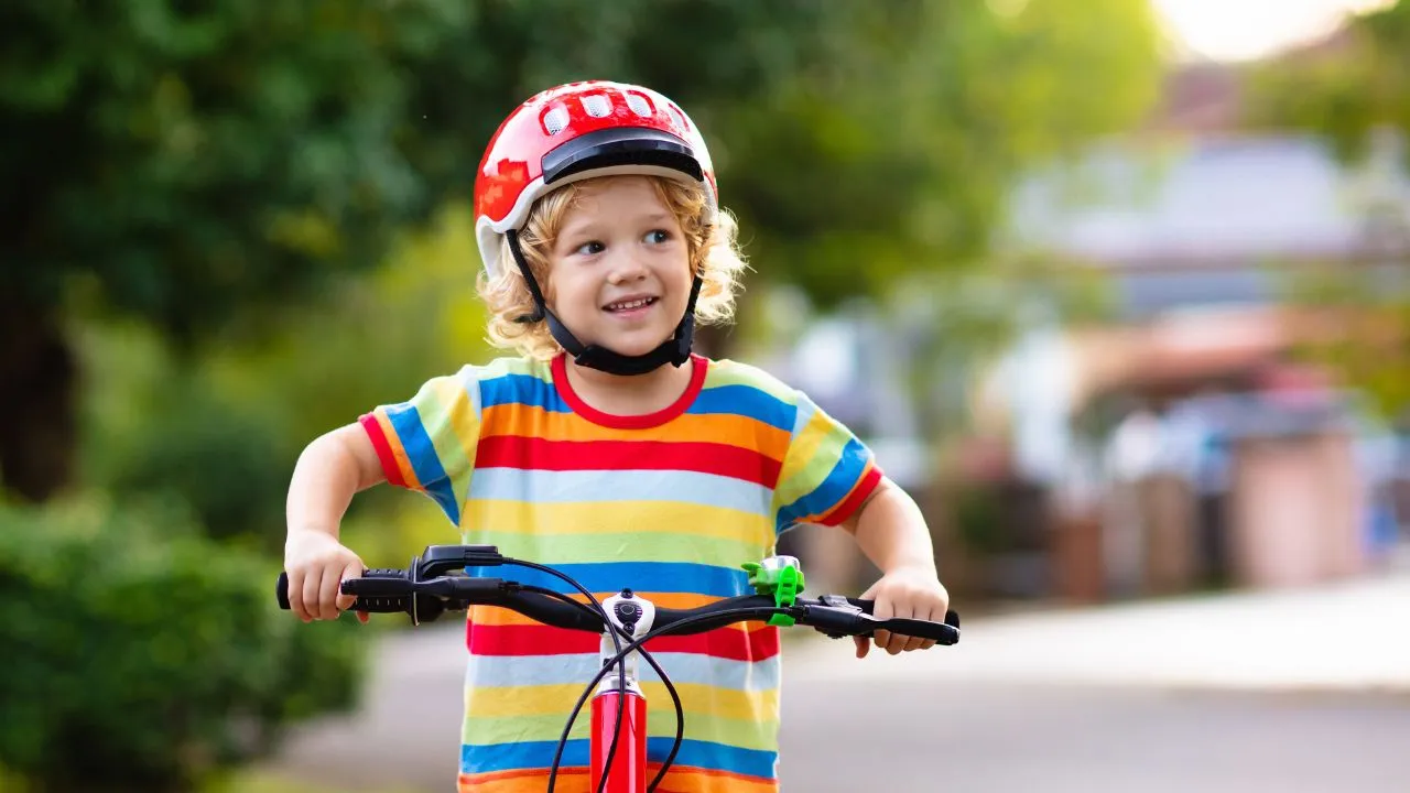 A young boy wearing a helmet rides his bike, smiling as he enjoys a sunny day outdoors.