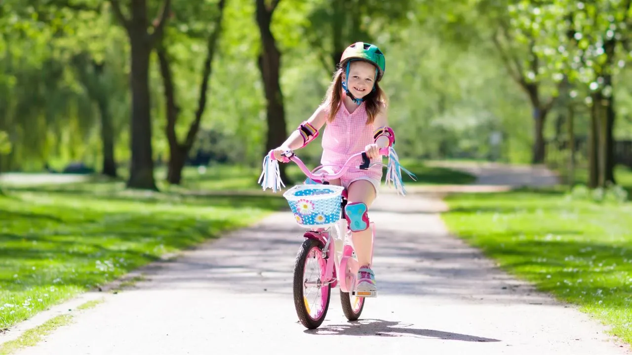 A young girl rides a pink bike along a scenic path, enjoying a sunny day outdoors.