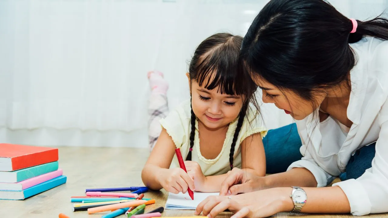 A woman and a child are focused on drawing together on a piece of paper at a table.