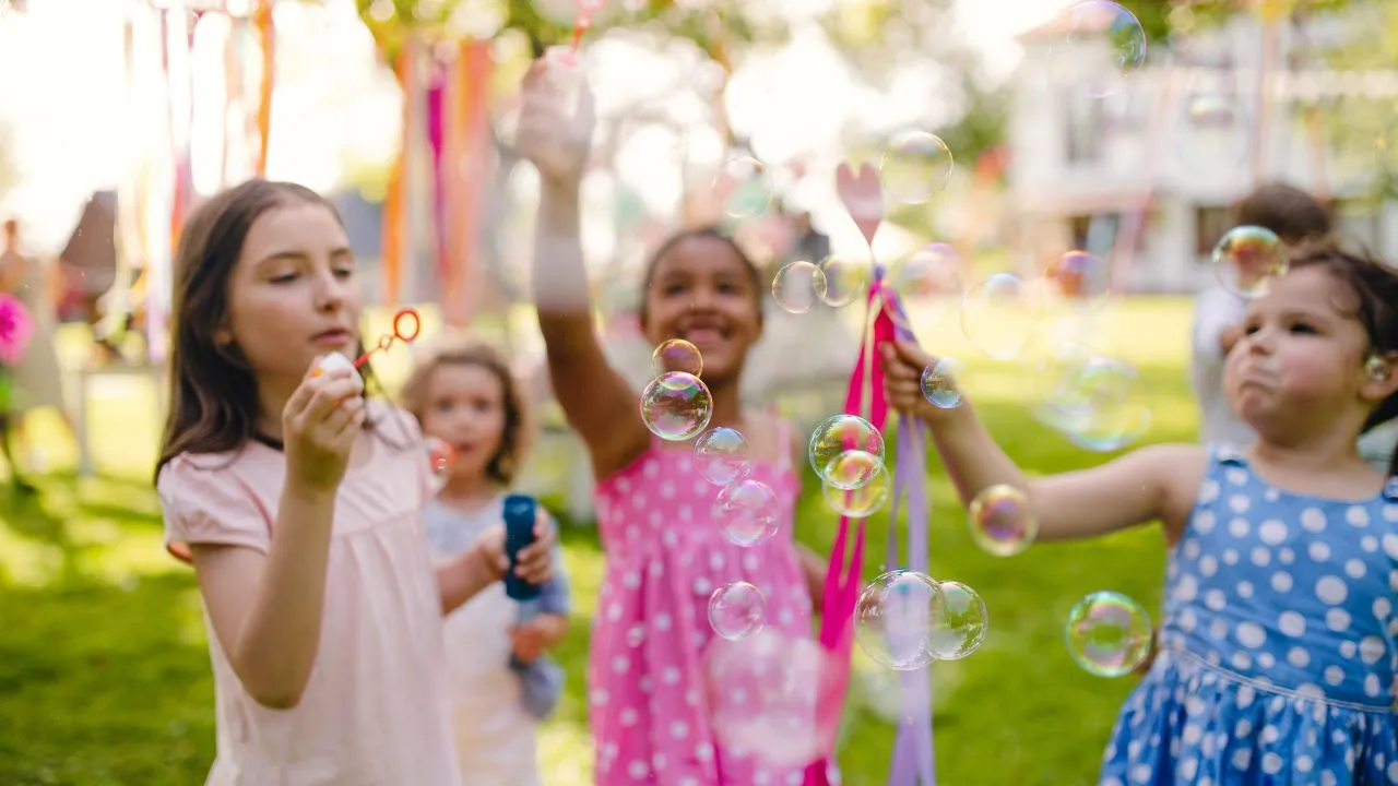 A group of children joyfully playing with bubbles on a sunny day in a grassy field.