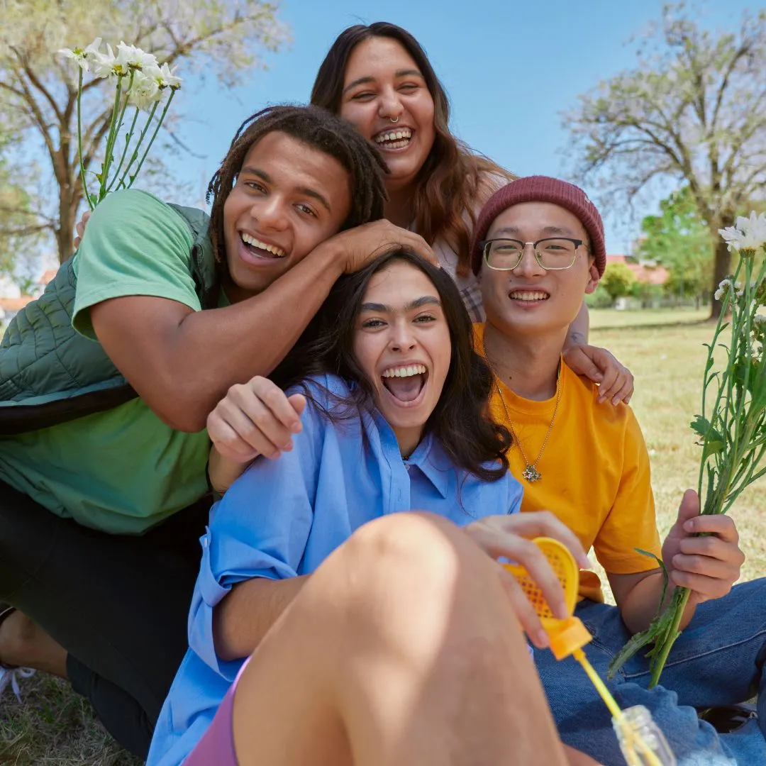  Four young people sitting on grass surrounded by colorful flowers, enjoying a sunny day outdoors.