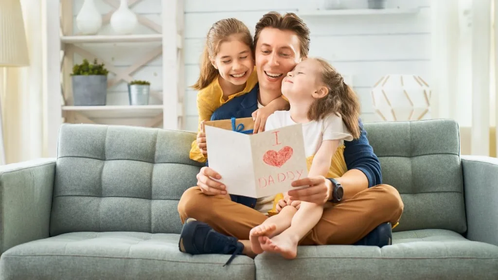 A joyful father and daughter share a moment reading a card together, smiling and enjoying their time.