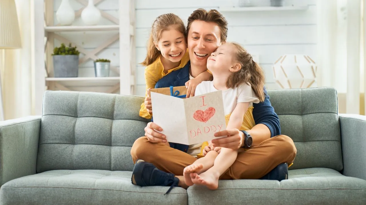 A joyful father and daughter share a moment reading a card together, smiling and enjoying their time.