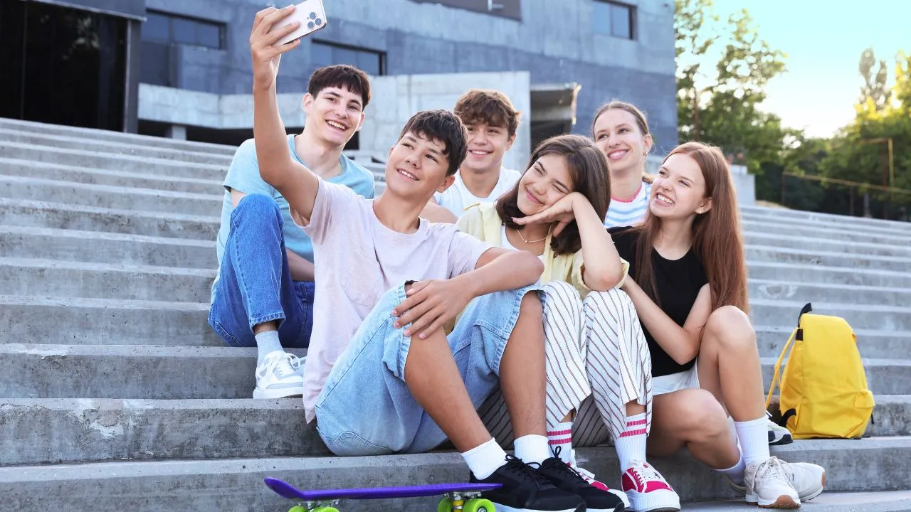 A group of young people sitting on steps, smiling and taking a selfie together.