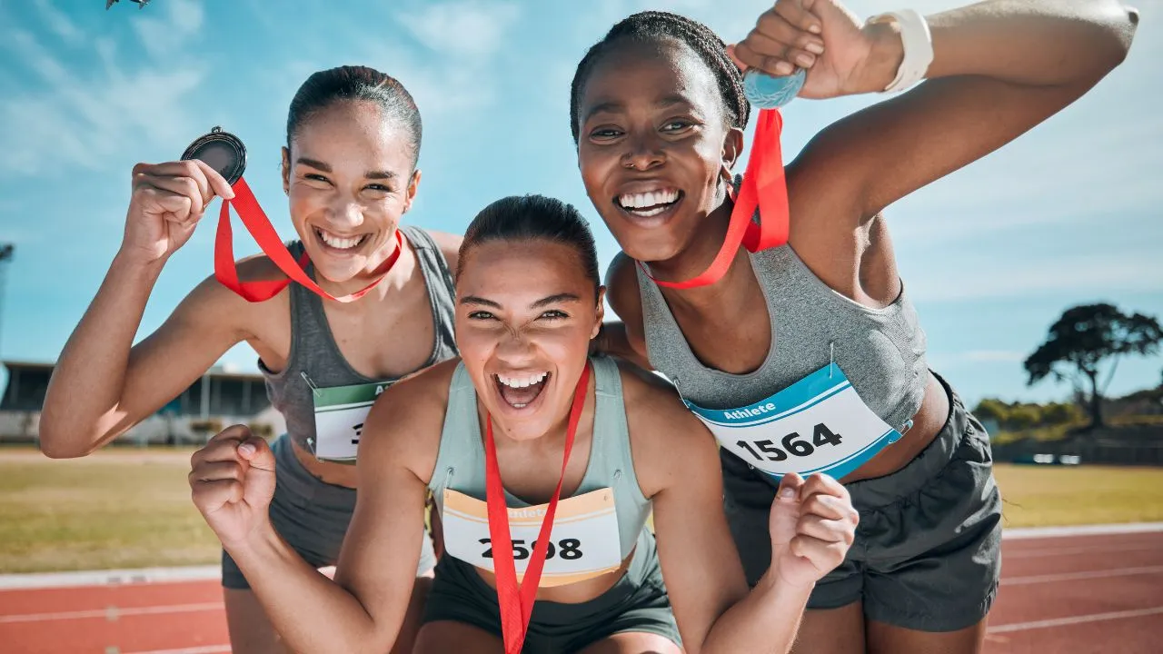 Three women proudly display their medals on a running track, celebrating their achievements in a race.