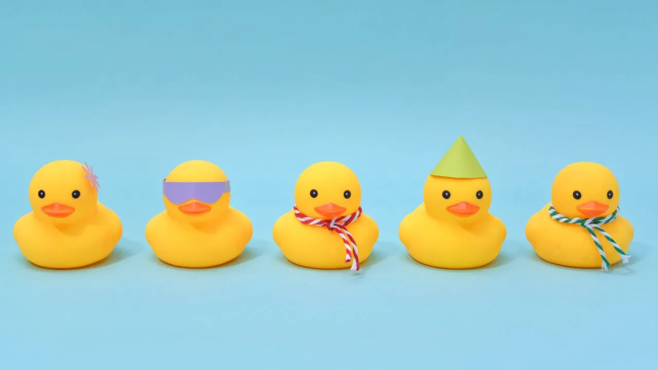 Five colorful rubber ducks in a row, each wearing a festive party hat, arranged on a white background.