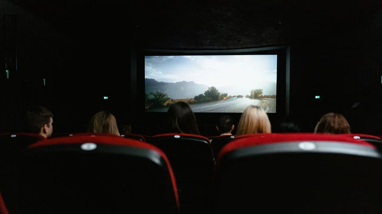 Audience members seated in a dark theater, focused on a movie screen in front of them.