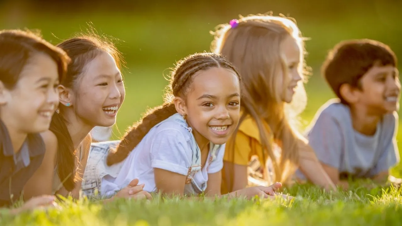 A group of children lying on the grass, enjoying a sunny day and playing together in a park setting.